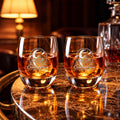 Two Moonlight Engraved Whiskey Glasses side by side with whiskey and round ice, each etched with the Chanter Vision crescent moon and boat emblem